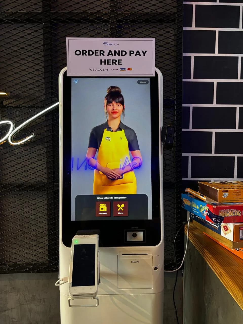 Order-and-pay kiosk with a Thrifty AI host on screen in a café