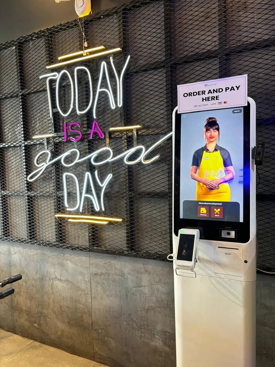 Thrifty AI kiosk beside a neon sign in a café