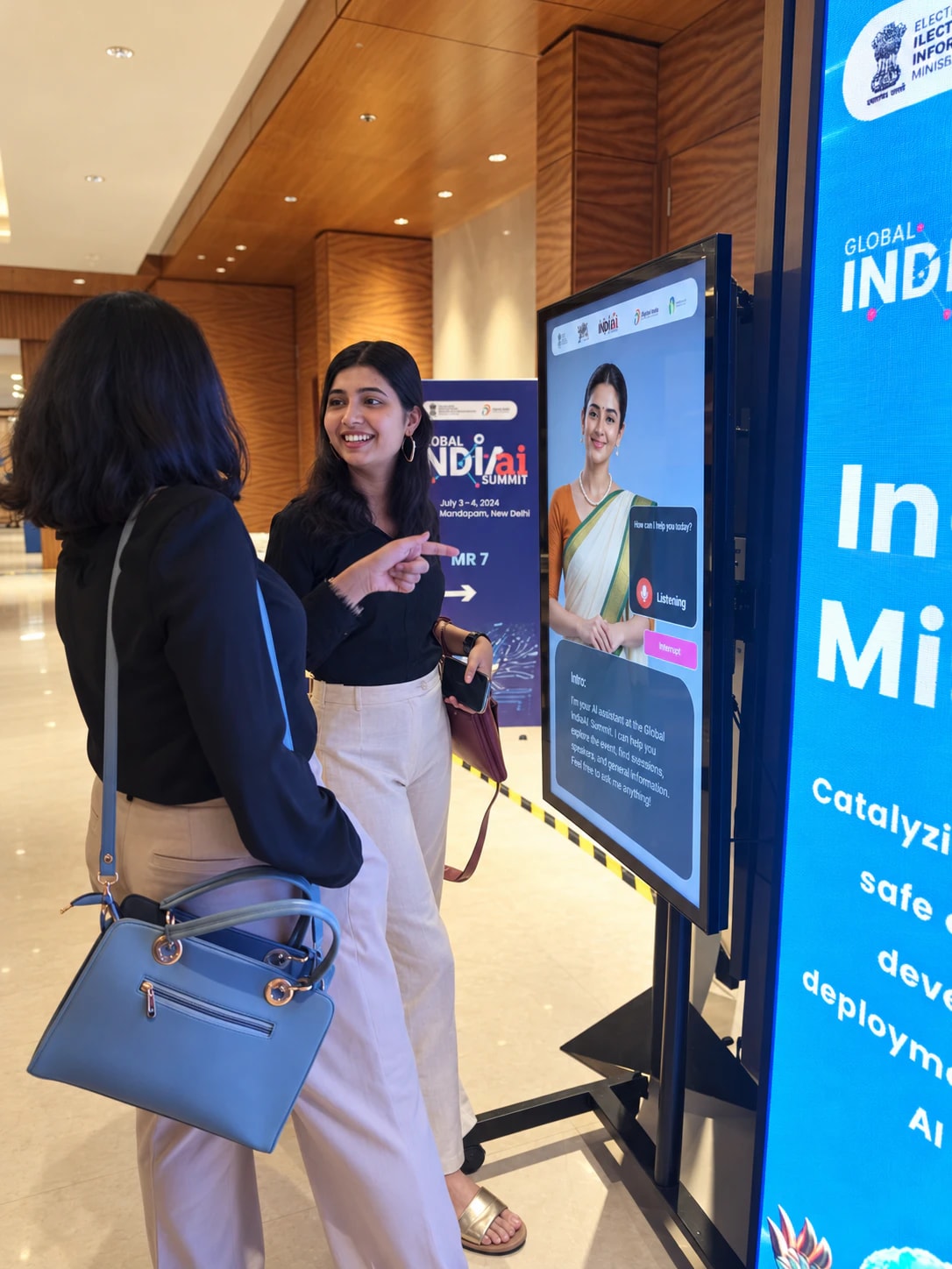 Two visitors at the Global IndiaAI Summit laughing as they talk to a Thrifty AI kiosk